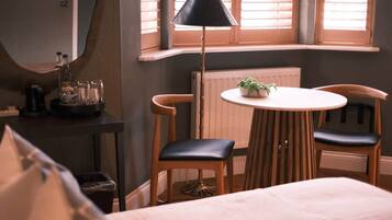 A bedroom with a bed, a round table with chairs, a lamp, and a window with blinds.