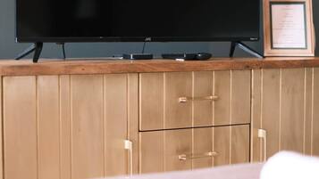 A television on a wooden cabinet with a remote control and a framed certificate.