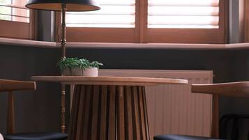 A room with a wooden table and two chairs, a lamp, and a window with blinds.