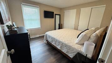A bedroom with a bed, a dresser, a television, and a window with blinds.
