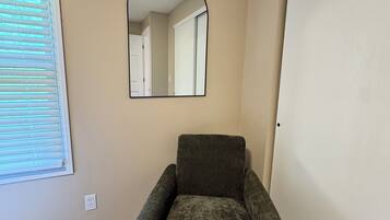 A room with a single armchair, a large mirror, a door, and a window with blinds.