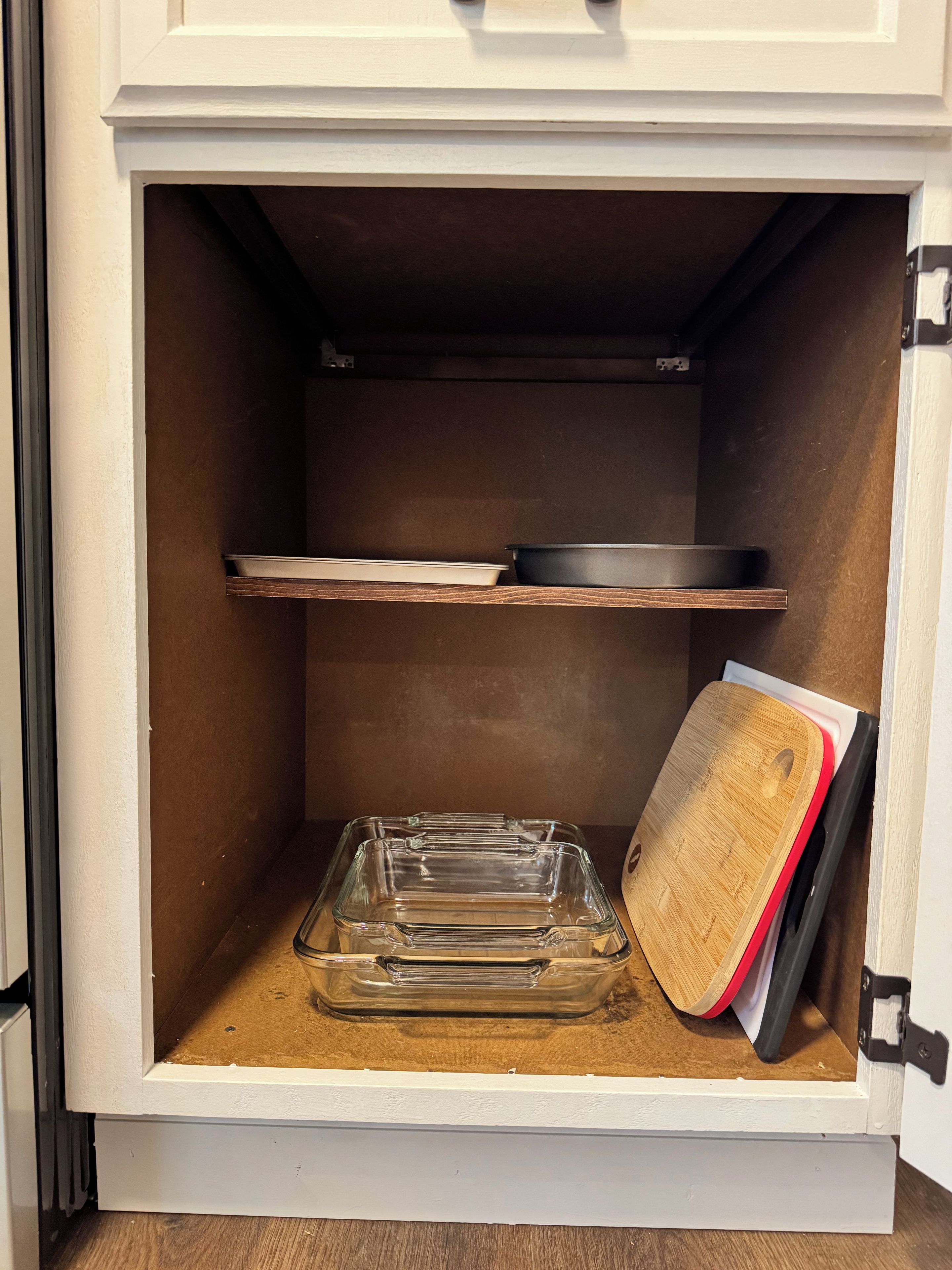 Un meuble de cuisine contenant un plat de cuisson en verre transparent et une planche à découper en bois.
