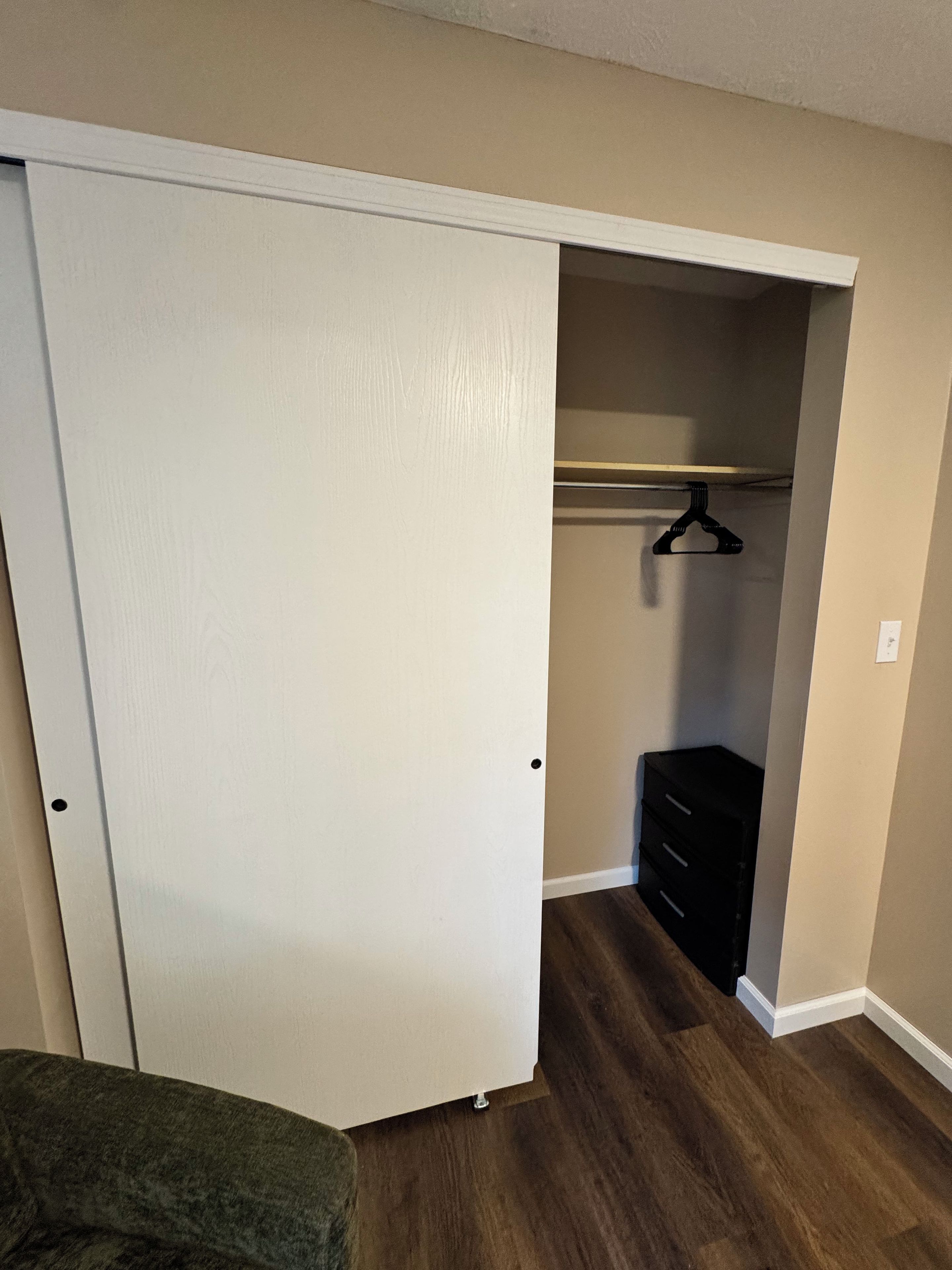 A room with a closed closet, a wooden floor, and a black dresser.