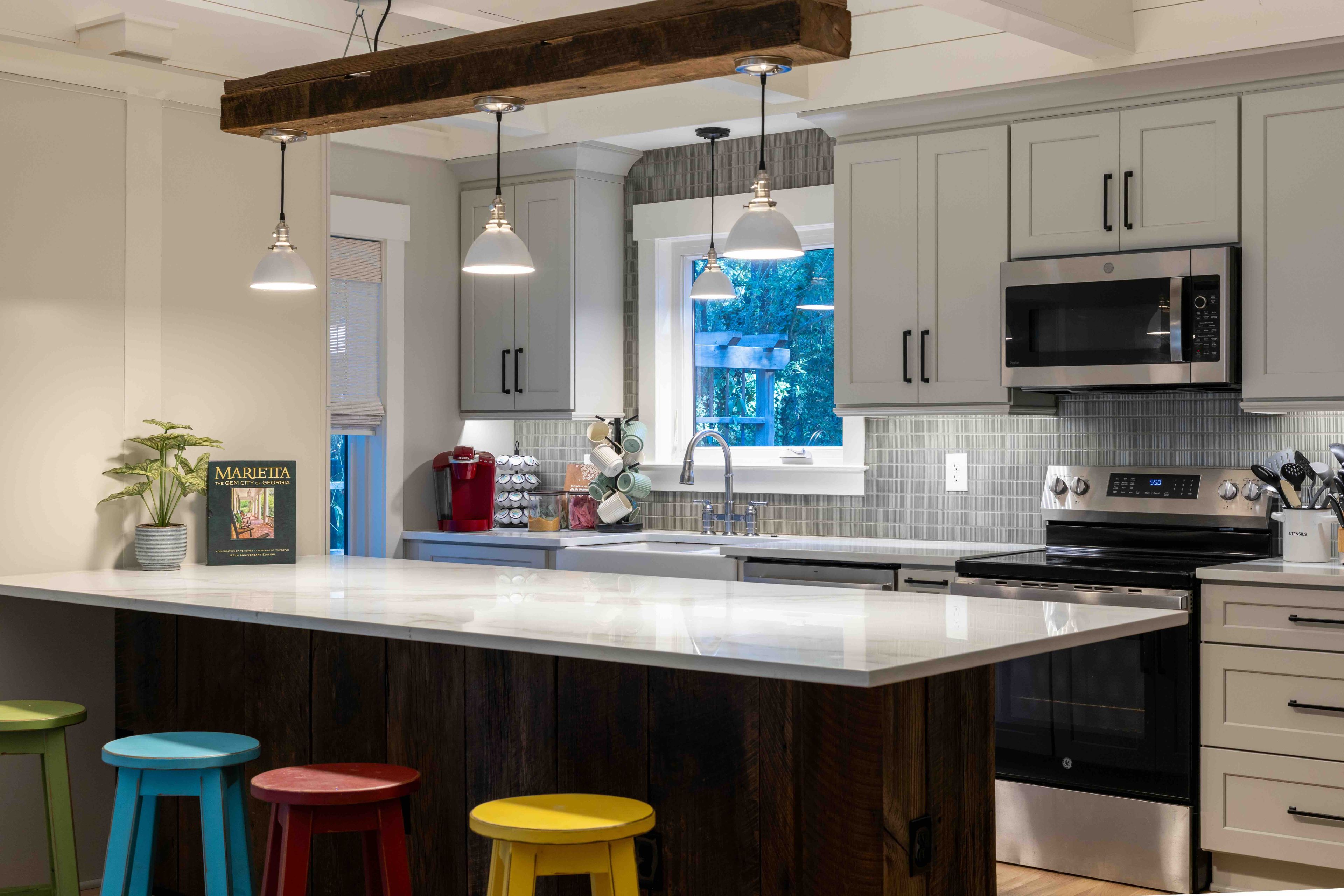 A modern kitchen with a central island, stainless steel appliances, and a window with a view of greenery.