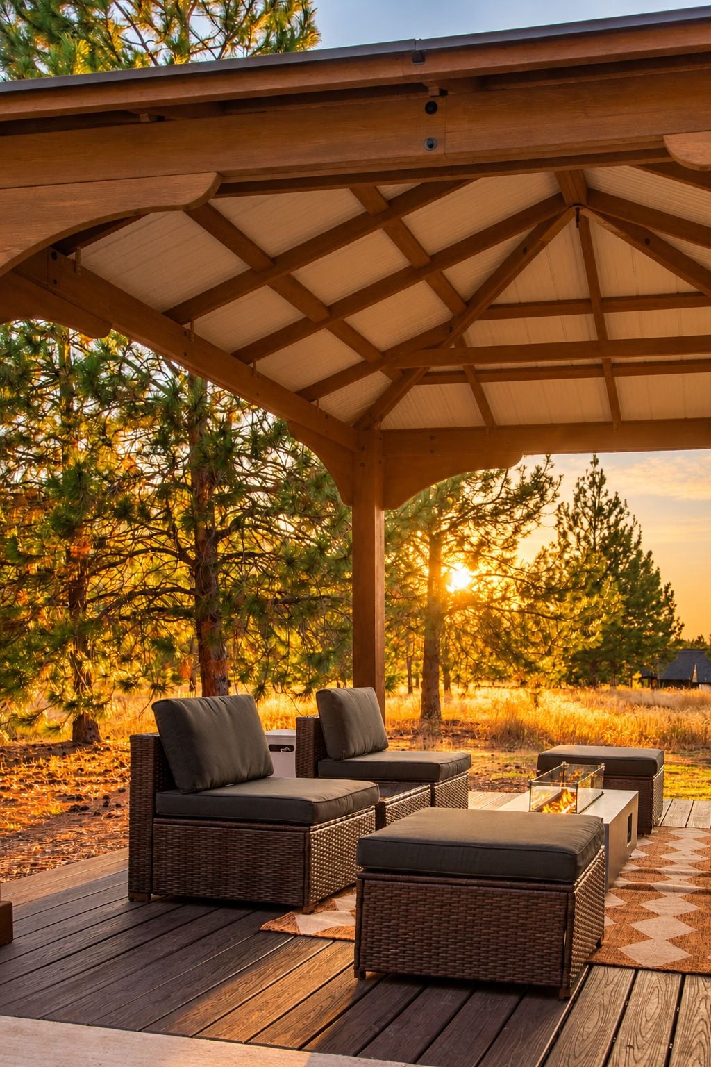 A covered outdoor seating area with wicker furniture and a view of trees and sunset.