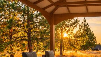 A covered outdoor seating area with wicker furniture and a view of trees and sunset.