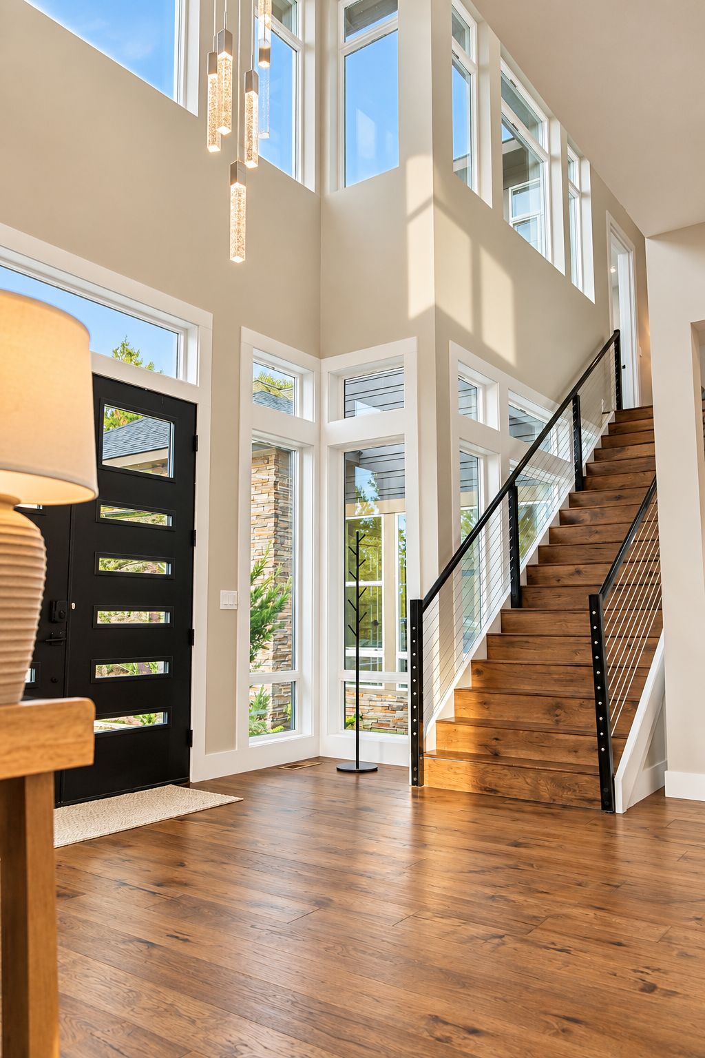 Un intérieur spacieux avec un escalier en bois, de nombreuses fenêtres et une porte noire.