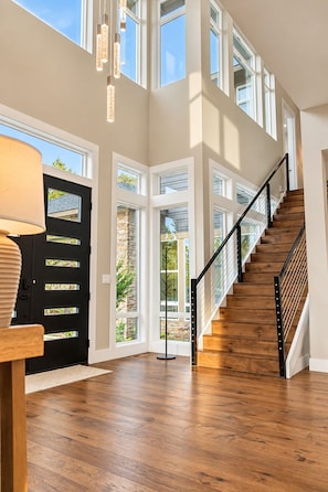 A spacious interior with a wooden staircase, multiple windows, and a black door.