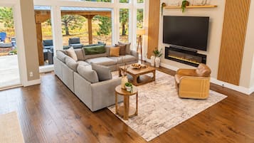 A modern living room with a sectional sofa, a flat-screen TV, a fireplace, and a large window overlooking a garden.