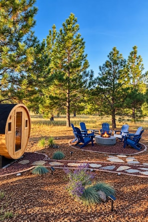 Una cabaña de madera con un ventanal circular, rodeada por un brasero y sillas Adirondack.
