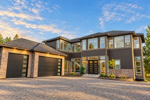 Une maison moderne à deux étages, dotée d’un garage, de grandes fenêtres et d’une allée gravillonnée.