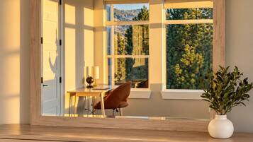 A room with a large window, a desk, a chair, and a vase with plants.