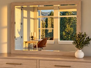 Une pièce avec une grande fenêtre, un bureau, une chaise et un vase avec des plantes.