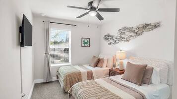 A bedroom with two beds, a ceiling fan, a TV, a window with blinds, and a wall decoration.