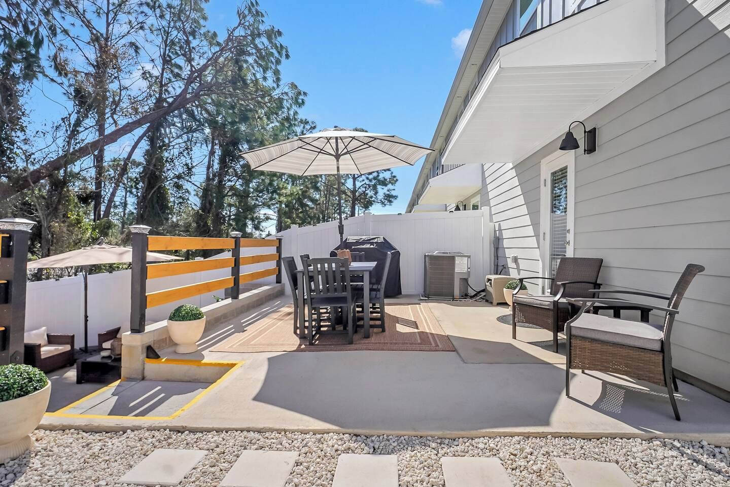 Un espacio de patio al aire libre con mesa y sillas, una parrilla y un gran paraguas.