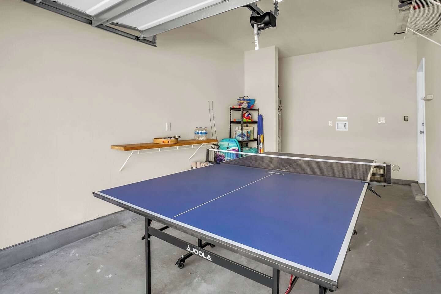 A ping pong table in a room with a shelf and a small collection of items on the wall.