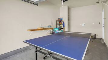A ping pong table in a room with a shelf and a small collection of items on the wall.