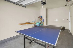 Uma mesa de pingue-pongue em um quarto com uma estante e alguns objetos expostos na parede.