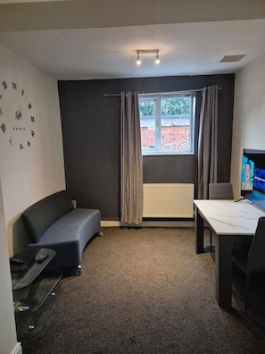 A compact room with a grey sofa, a small table, a TV, and a window with curtains.