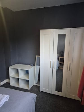 Ein Schlafzimmer mit einem Bett, einem weißen Kleiderschrank mit Spiegeln, einem Schreibtisch und einem Stuhl.