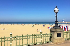 Ein Strand mit einem grünen Zaun, einem Laternenpfahl und einer Flagge.