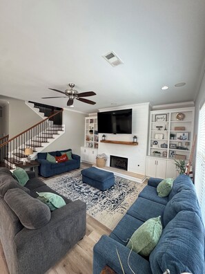 A modern living room with a staircase, a flat-screen TV, and a fireplace. - Spacious 6-bedroom house with 2 Owner’s Suites in Evans-Riverwood (Evans)