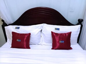 A bed with white linens and two red pillows with a logo, set against a dark wooden headboard. - Vine Inn Mbarara (Mbarara)