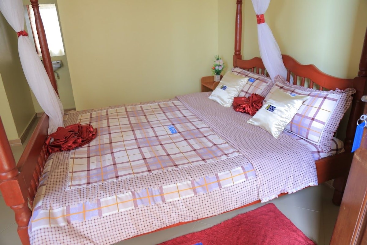 A four-poster bed with a checkered bedspread, pillows, and a red throw blanket.