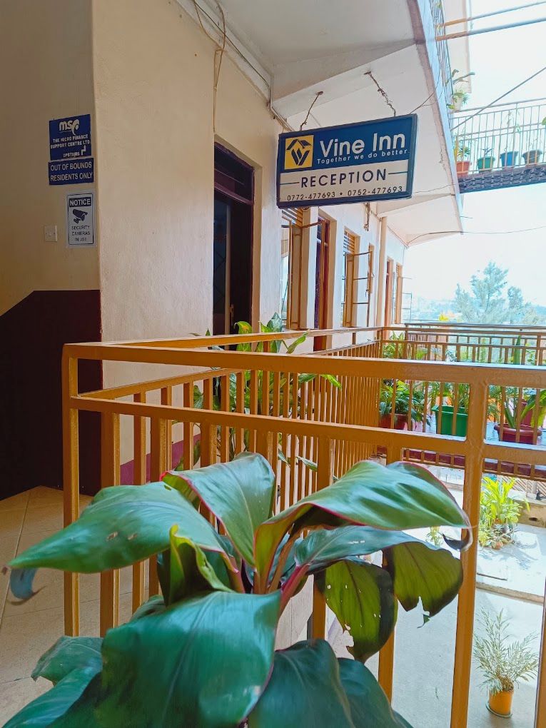 A reception area with a sign for Vine Inn, a security camera notice, and a balcony with potted plants.