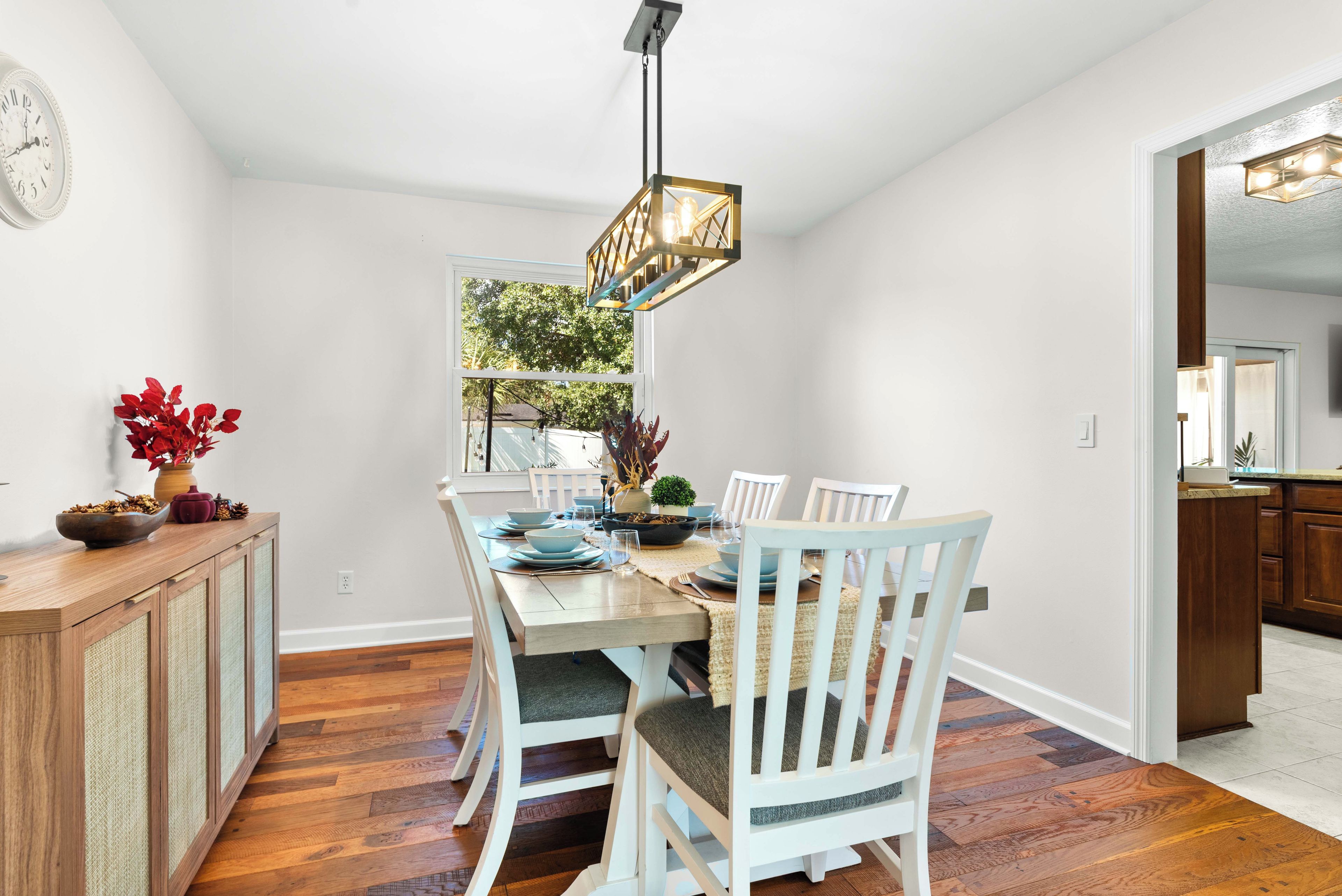 A dining area with a wooden table, white chairs, and a hanging light fixture.