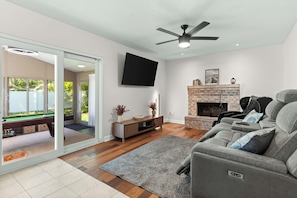 A modern living room with a flat-screen TV, a fireplace, a pool table, and a ceiling fan. - Mayo Guests - Relax with Massage Chair, Pool Table, Fire pit & Yard. (Jacksonville)