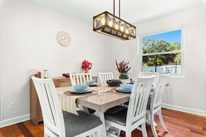 A dining area with a wooden table, white chairs, and a hanging light fixture.