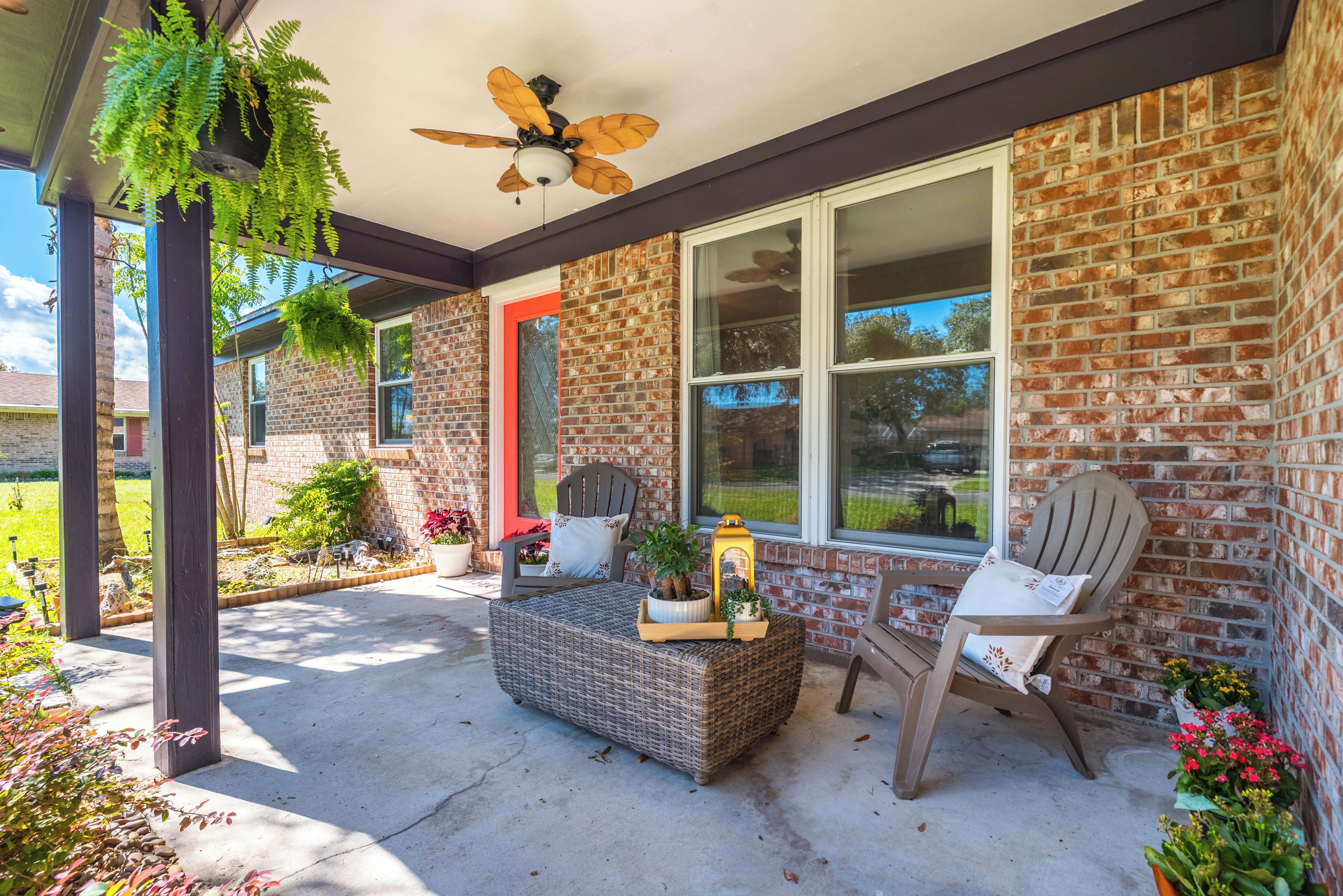 A covered porch with a brick wall, a ceiling fan, and two wicker chairs.