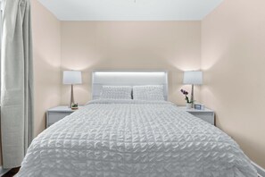 A neatly made bed with a white duvet, two bedside lamps, and a small potted plant on the nightstand.