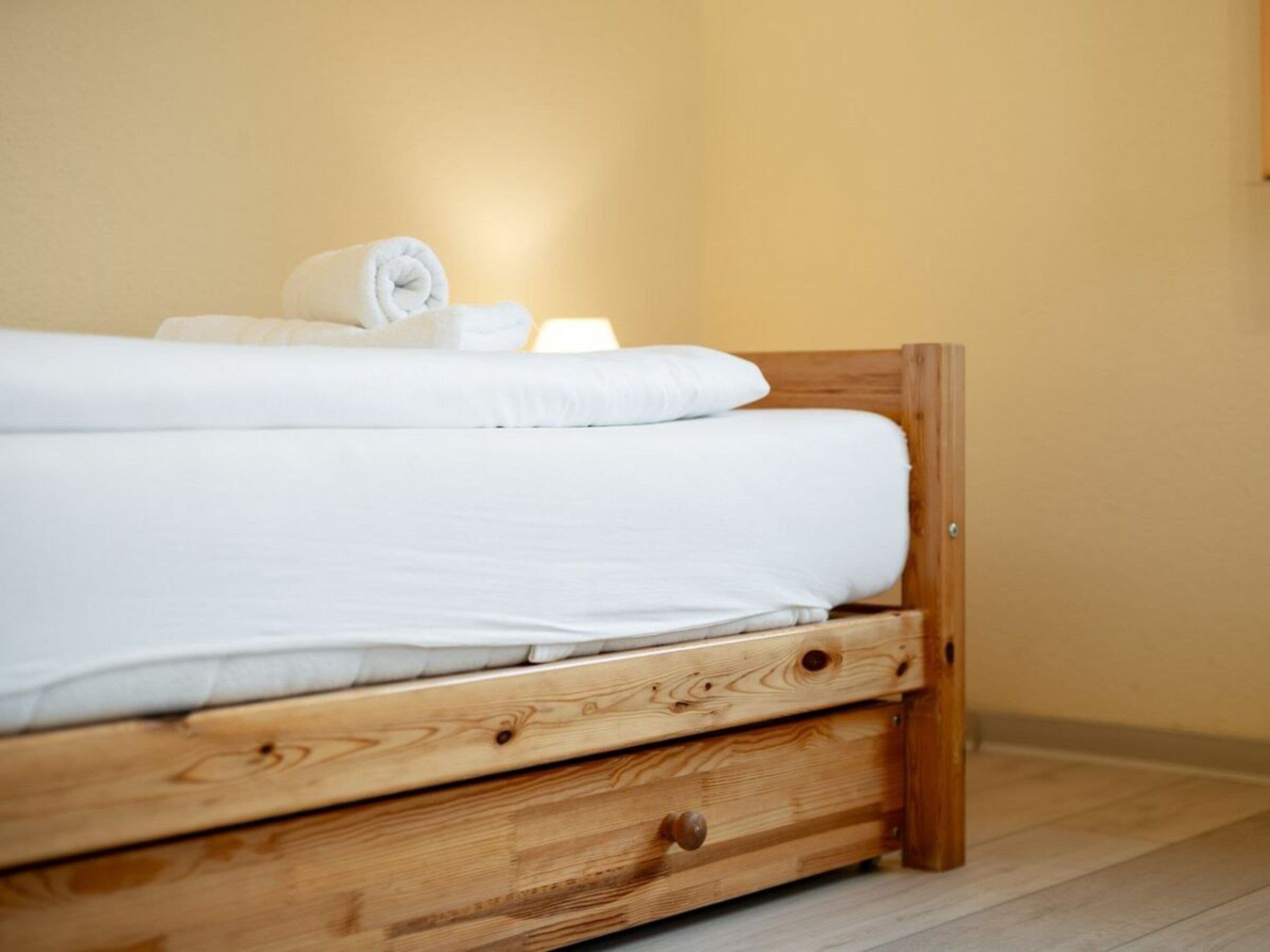 A single bed with a wooden frame and a wooden drawer below it.