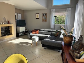 A modern living room with a sectional sofa, a flat-screen TV, a fireplace, and a large window with curtains. - New Listing (Epagny Metz Tessy)