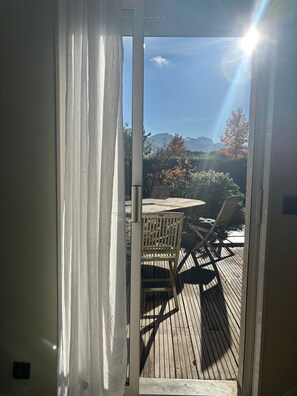 Um deck de madeira com mesa e cadeiras, vista para montanhas e céu claro.