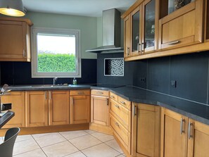 A kitchen with wooden cabinets, a black countertop, a window with a view of greenery, and a tiled floor. - New Listing (Epagny Metz Tessy)