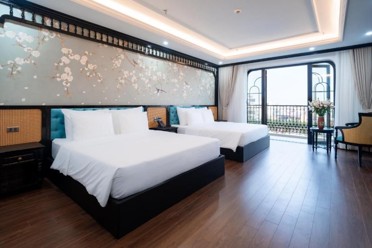 Quarto de hotel com duas camas, uma varanda e uma vista, além de um detalhe decorativo na parede.