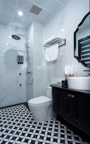 Casa de banho moderna com sanita branca, chão com padrão preto e branco, toucador preto com espelho e cabine de duche com teto branco.