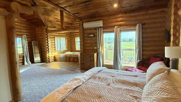 Quarto de cabana de madeira com uma cama grande, teto de madeira e vista para uma paisagem verde pela janela.