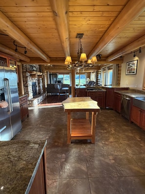A spacious kitchen with a central island, wooden ceiling beams, and a stone fireplace.