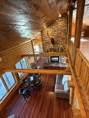 A wooden interior with a stone fireplace, a round table with chairs, and a sofa.