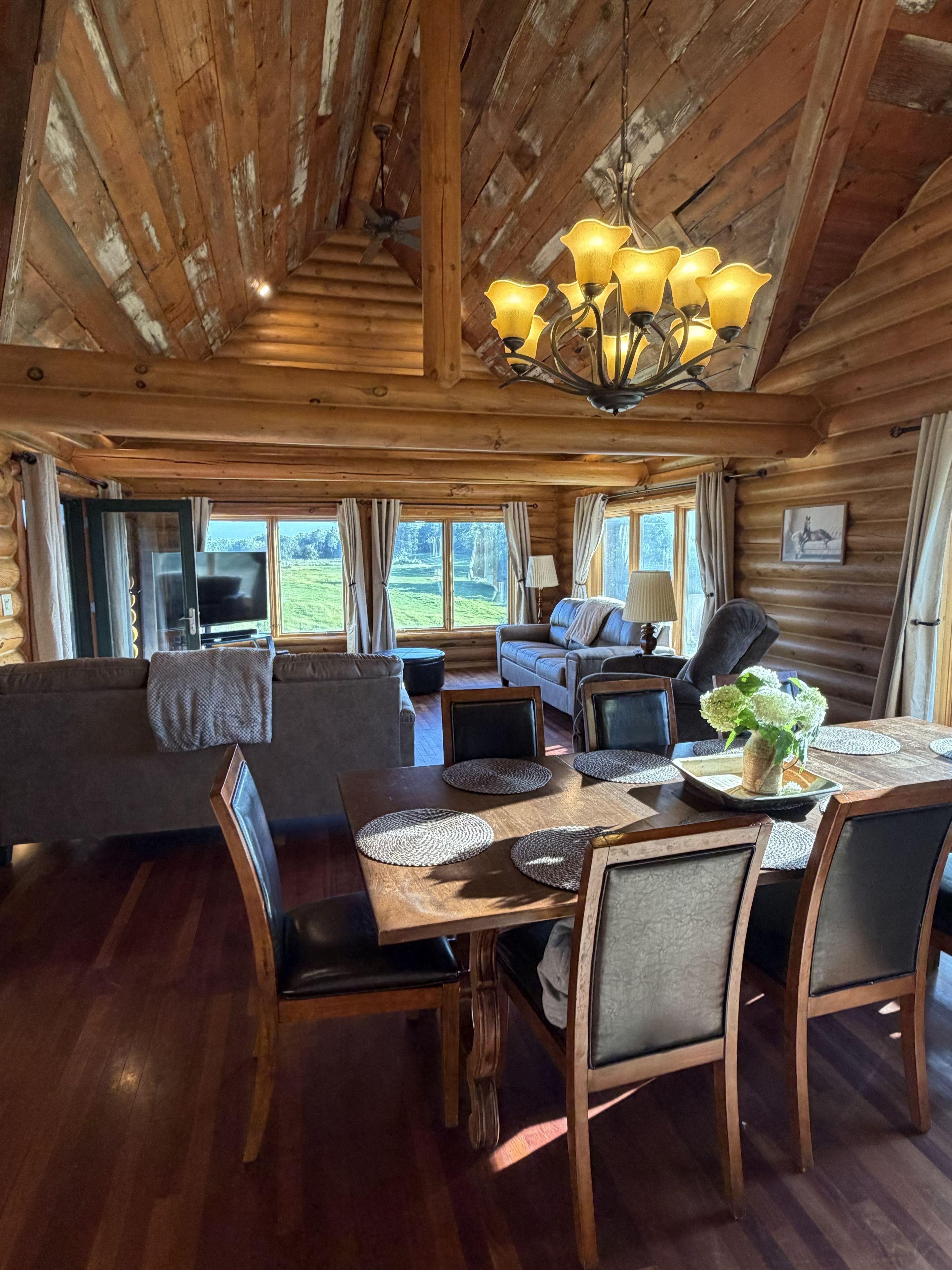 A cozy cabin interior with a wooden dining table, chairs, a sofa, and a television.