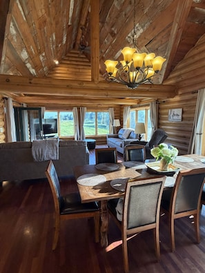 A cozy cabin interior with a wooden dining table, chairs, a sofa, and a television. - High Country Ranch 4300 sf Log Home, 4 bedrooms (La Crescent)