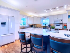 Una cocina moderna con armarios blancos, una isla central con taburetes altos y un ventanal que proporciona luz natural.