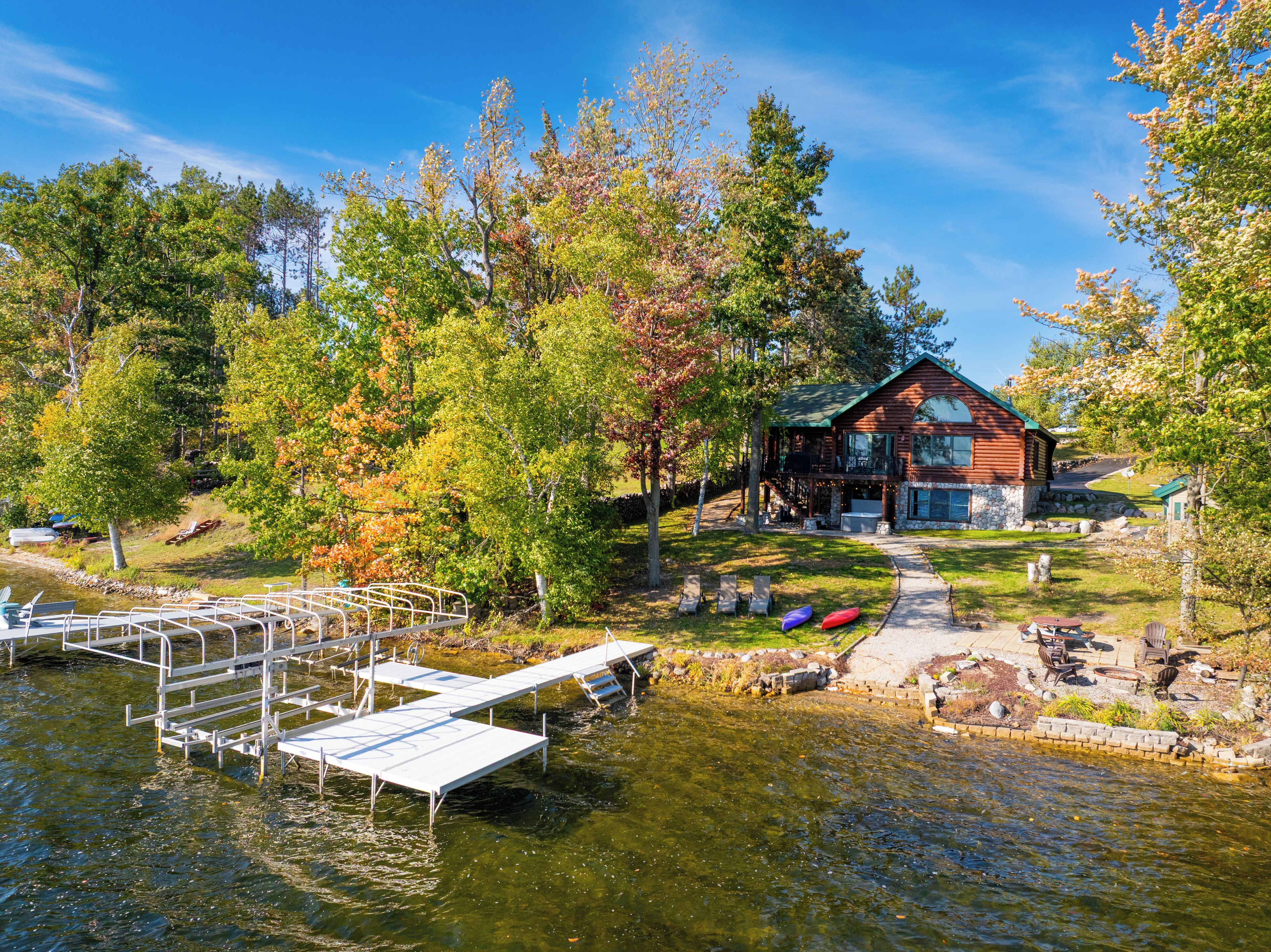 A cabin with a dock extending into a lake, surrounded by trees with autumn foliage.