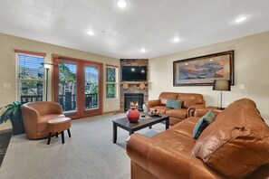 A living room with leather sofas, a fireplace, a flat-screen TV, and a large window with blinds. - 2BR Moose Hollow Condo 1402 | Pool, Hot Tub & Sauna (Eden)