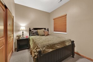 Une chambre à coucher avec un lit, une table de chevet, une lampe et une fenêtre avec des stores.