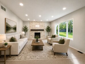 A living room with a fireplace, sofas, a coffee table, and a large window. - Luxury Furnished Home - 90 Day Minimum Stay (Lincoln)